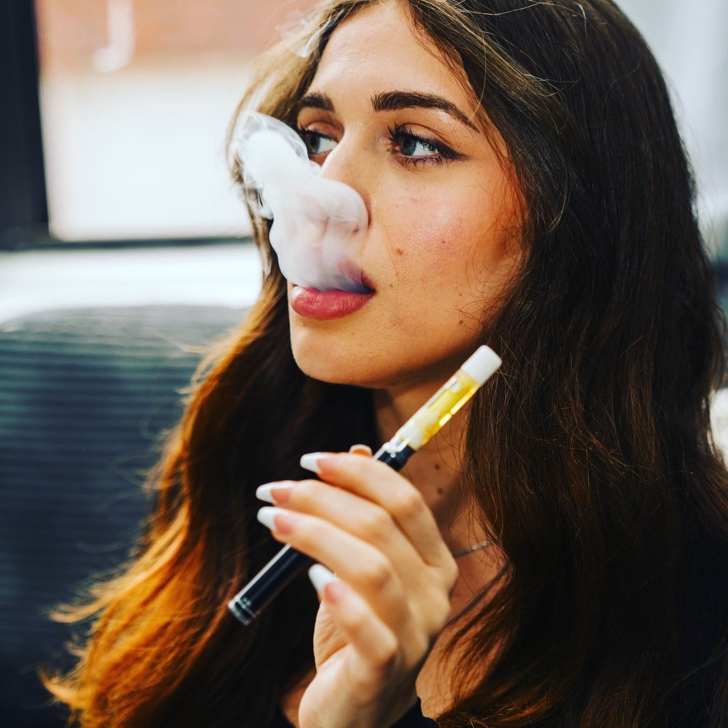Woman exhaling vapor from black and gold vape pen