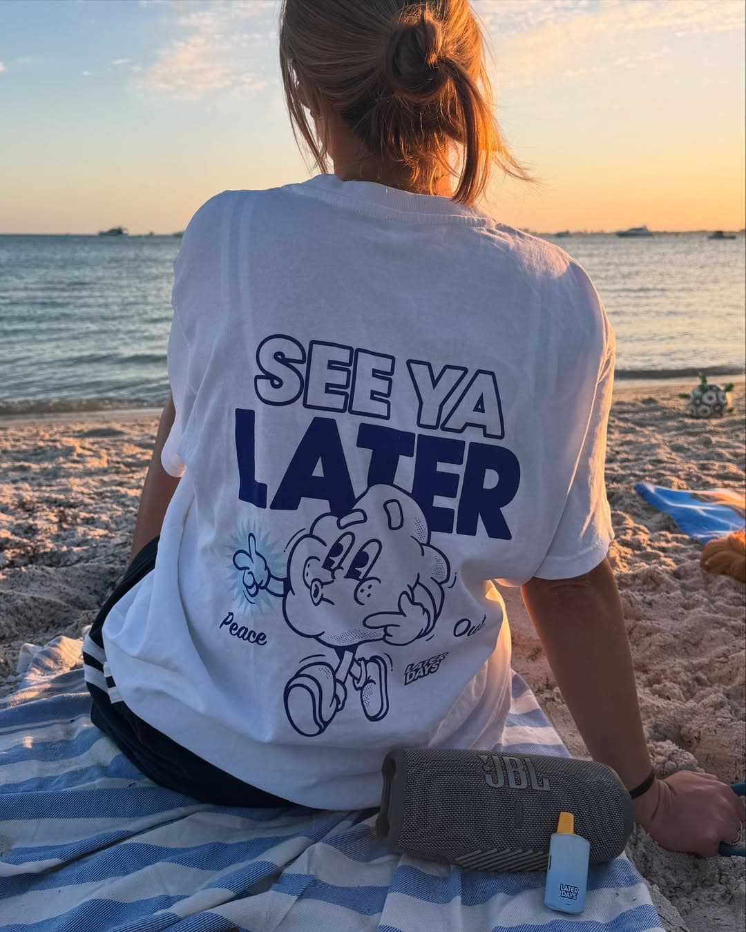 Woman wearing a Later Days See Ya Later tee relaxing at the beach in New Jersey