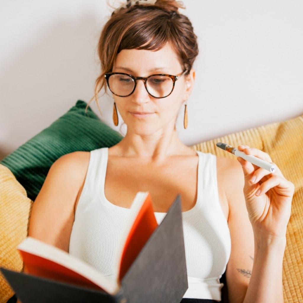 Woman in glasses holding a cannabis pen on a yellow couch